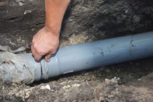 Hand fitting gray PVC pipe connection in a trench for drainage system
