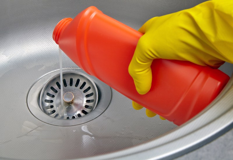A Professional Plumber Pours Sewer Pipe Cleaner Down the Kitchen Sink Drain in Illinois