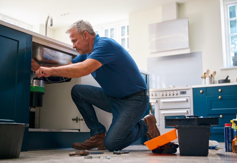 Male Plumber Fixing Waste Disposal Unit under a Kitchen Sink in Illinois