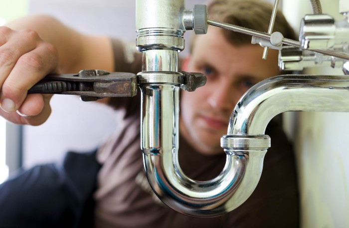 Plumber tightening under-sink pipe with wrench during emergency repair in Naperville, IL