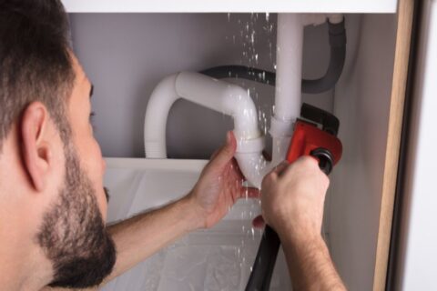 Plumber repairing a leaking pipe beneath a sink