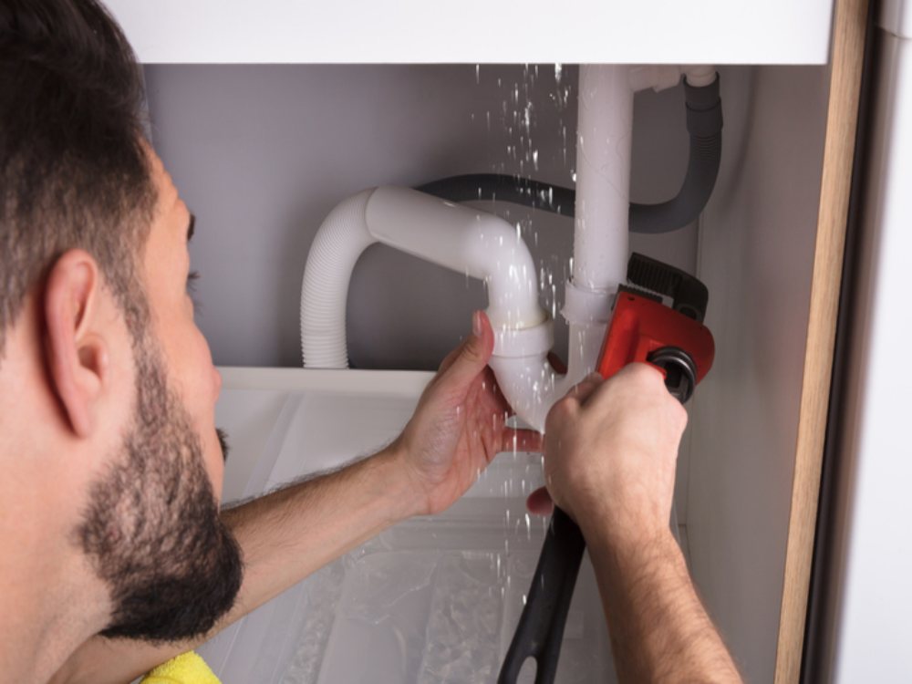 Plumber repairing a leaking pipe beneath a sink